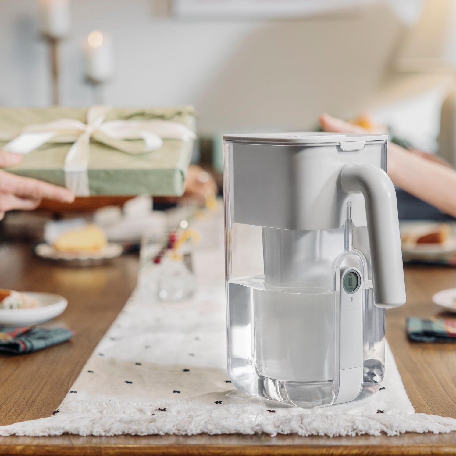Clear water filter pitcher on a table with a blurred background of people and food.