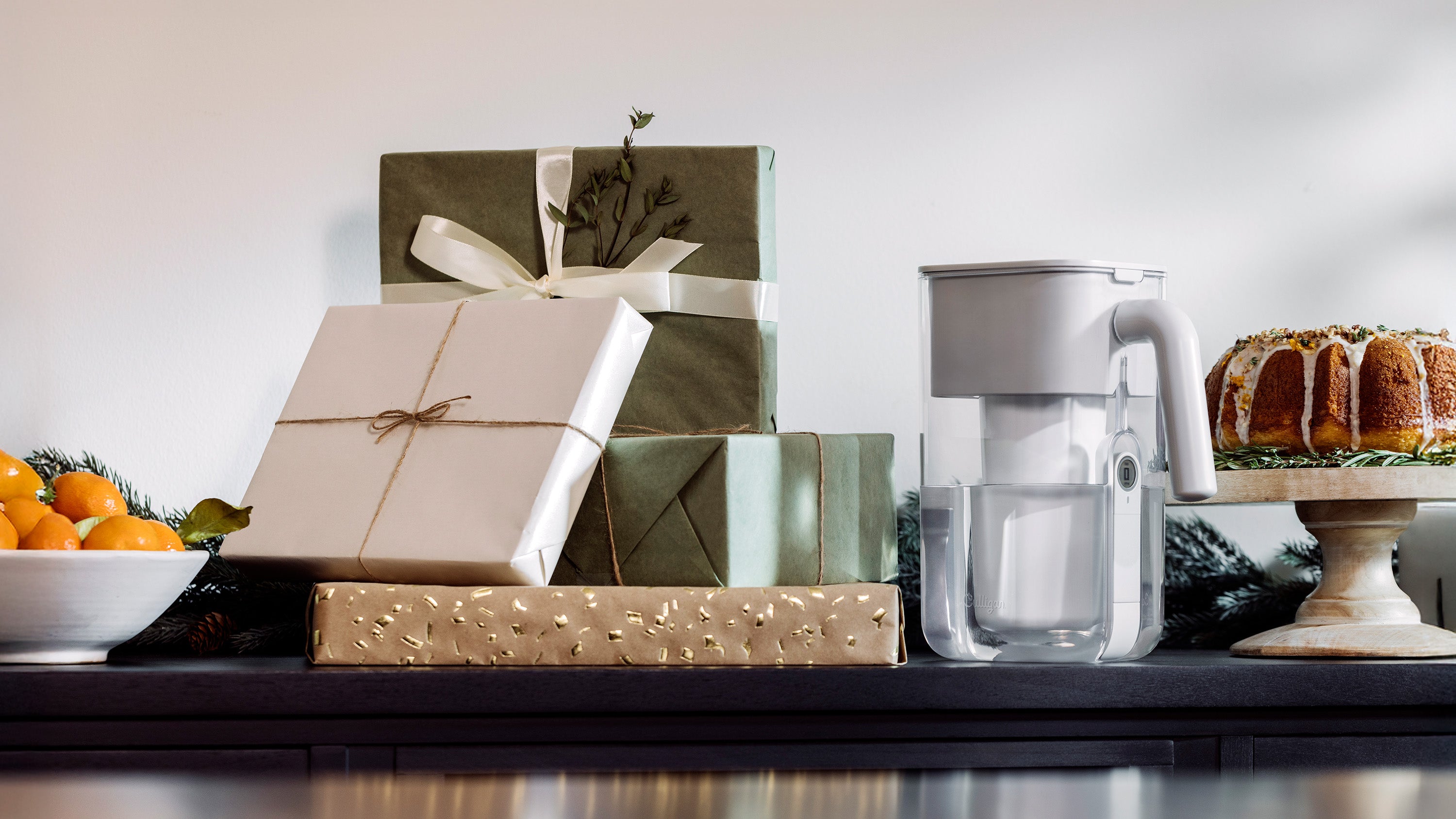 Gifts wrapped in brown paper with string, a water filter, and a cake on a table.